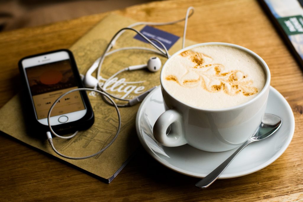 A coffee table with a cellphone, cup of coffee, and a pair of headphones.