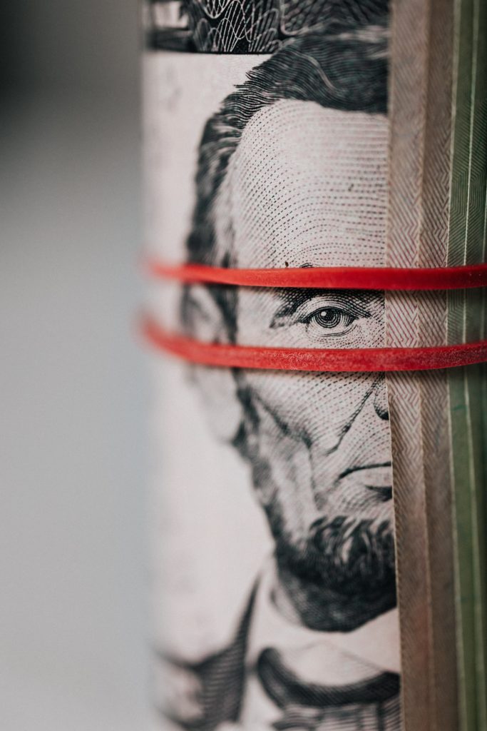 A close up of a roll of dollar bills with a red elastic band around it.