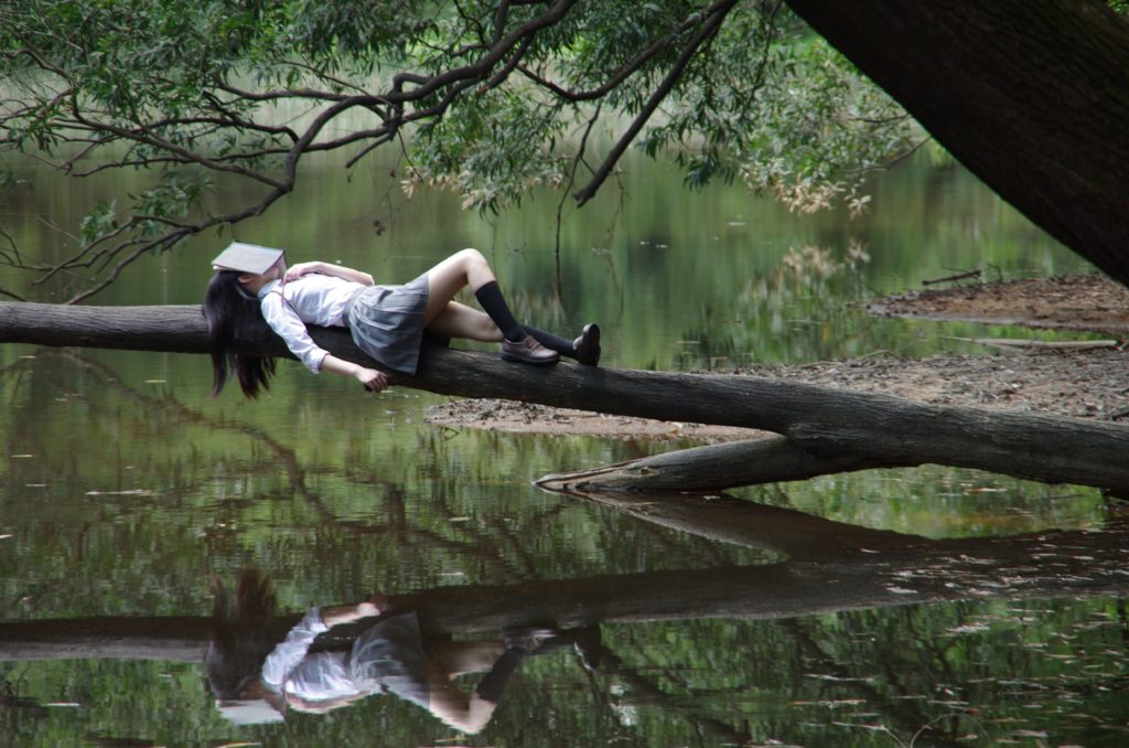 A girl relaxing on tree over a lake with her head in a book