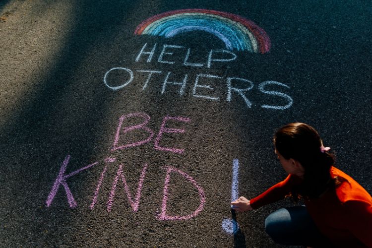 A woman writing the words: "Help others , Be Kind!" on a road in chalk.