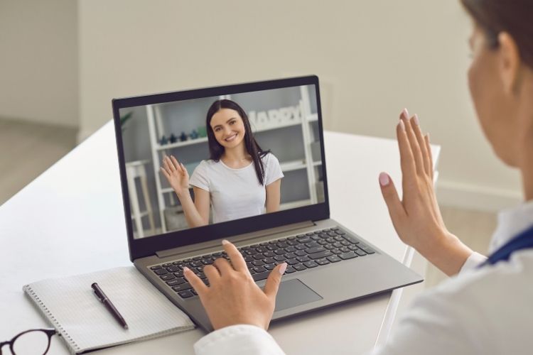 A person on a video call waving to the person on the laptop screen.