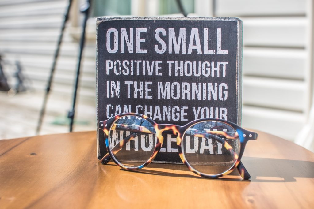 A tabletop with a pair of spectacles and a sign with the words: One small positive thought in the morning can change your whole day".