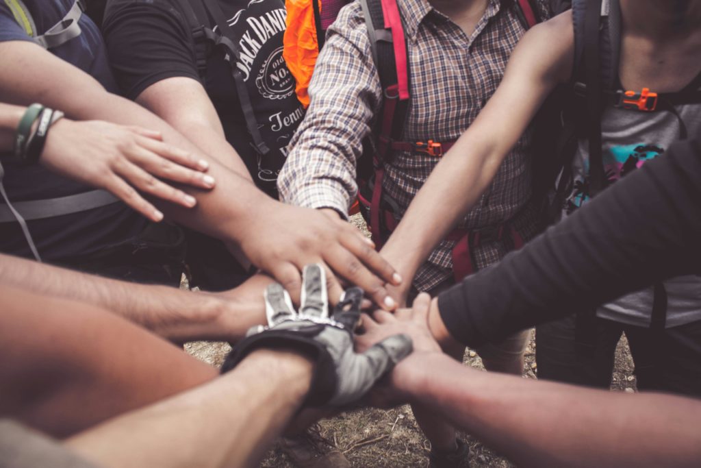 A group of people all putting their hands together in a circle, depicting trust and teamwork