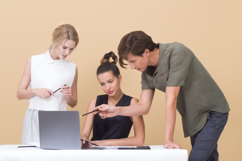 Three people having a discussion in front of a laptop