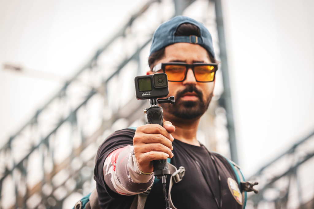 A man wearing sunglasses and a cap holding a GoPro camera on a gimbal.