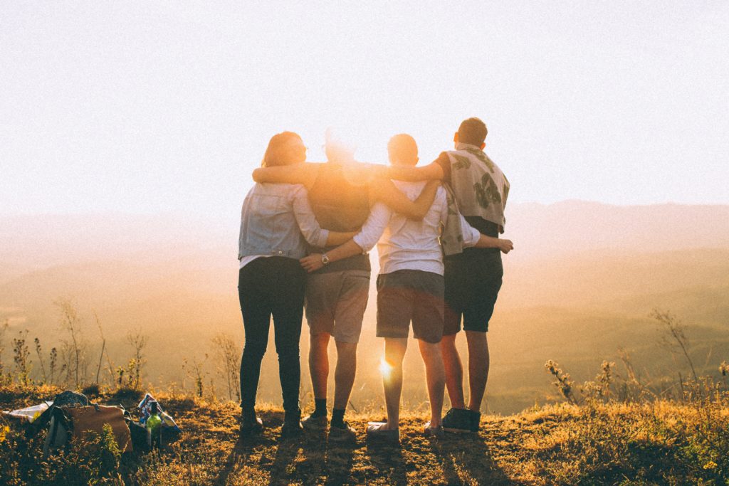 A group of friends standing arm in arm on top of a mountain.