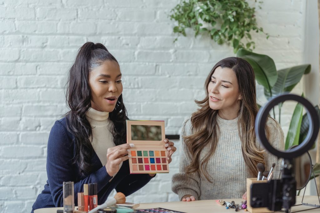 Two women discussing various make up products.