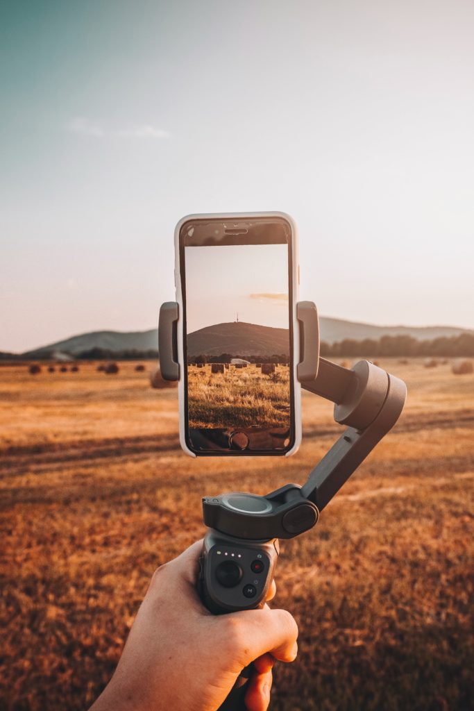 A cellphone on a gimbal being held up against a beautiful landscape.