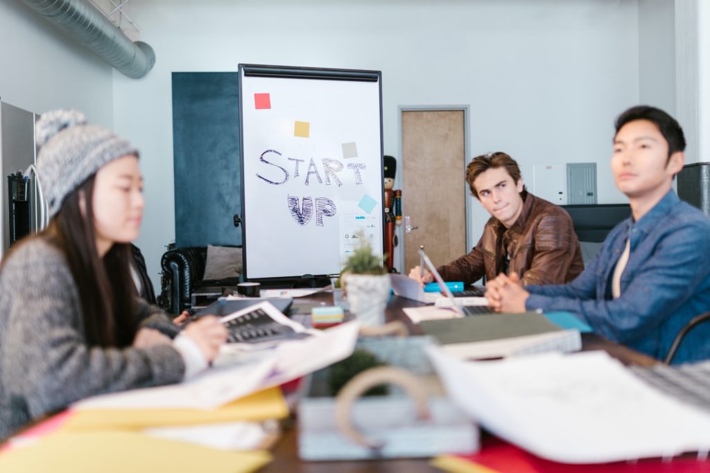 Three entrepreneurs sitting at a table with a flashboard with the words :" Start Up" on it.