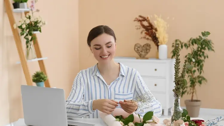 A florist sitting in front of her laptop while working with flowers. 