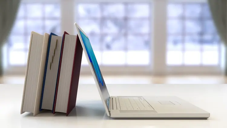 A stack of books leaning against an open laptop.