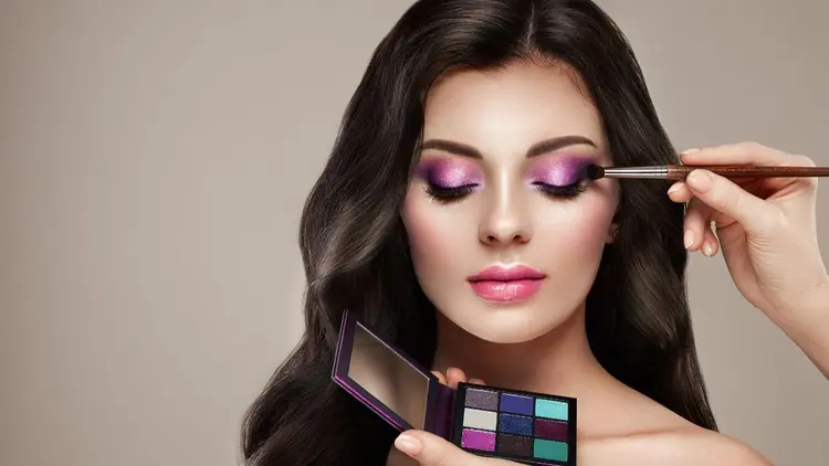 A woman having eye make up applied by a makeup artist.