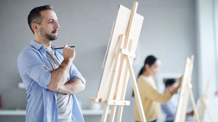 A man standing in front of an easel in an art class. 
