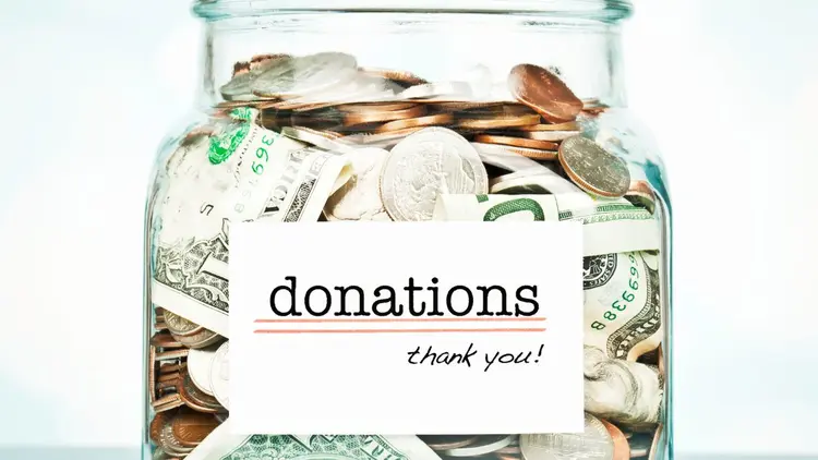 A Jar filled with coins and notes with the word: Donations-thank you!" printed on it.