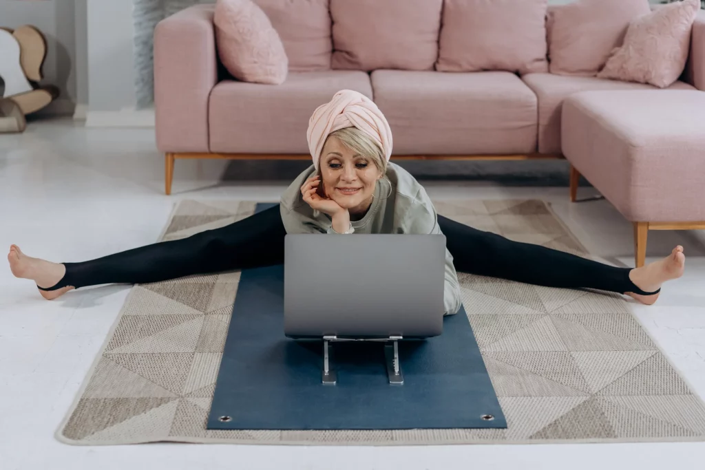 An older lady doing yoga in front of a laptop.