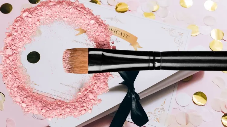 A makeup brush and powders in front of a certificate.