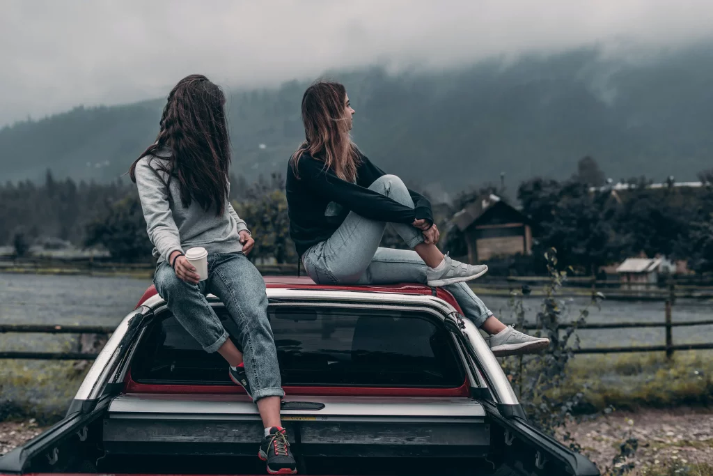 Two young women on top of a car, looking at the view ahead.