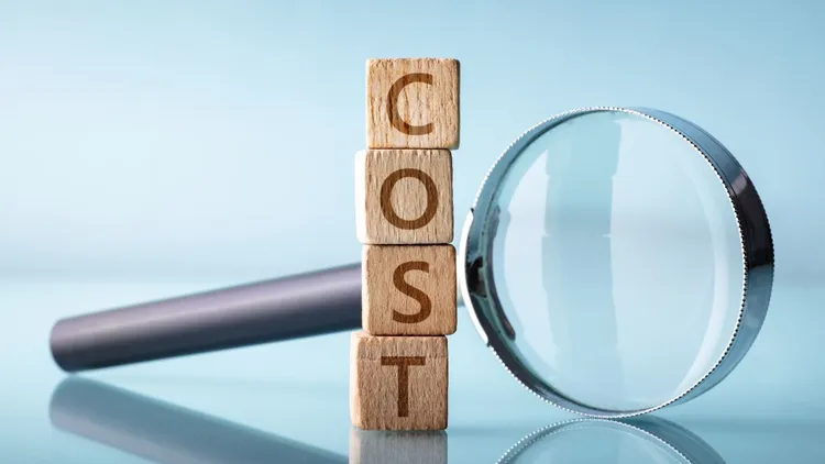 A stack of letter blocks spelling out the word "cost" next to a magnifying glass.
