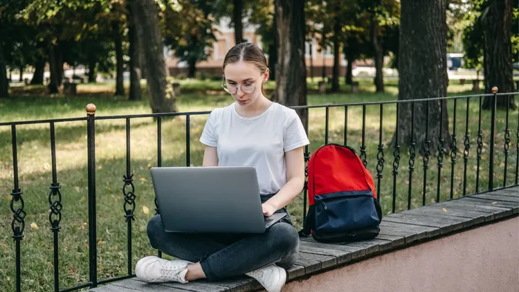 A lady sitting in a park while working on her laptop.