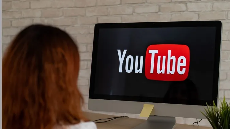 A woman sitting in front of a desktop computer with Youtube on the screen.