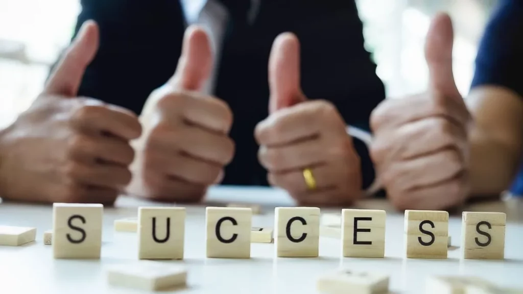 A team of people giving a thumbs up sign with the words "success" spelt out. 