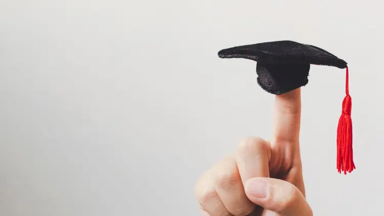 A tiny little graduation hat perched on top of a finger. 