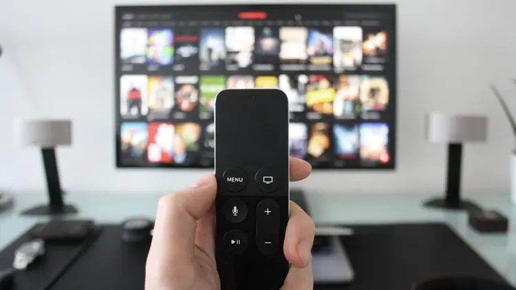 A close up of TV remote with TV in the background. 