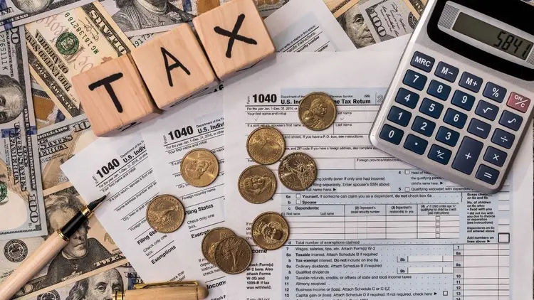 Tax paperwork, with coins and a calculator and letter blocks spelling the word "tax". 