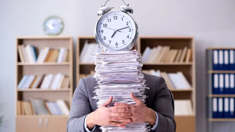 Someone holding a stack of paperwork with a clock on top of the stack. 