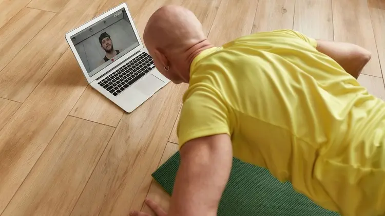 A man doing pushups while looking at a video on his laptop. 