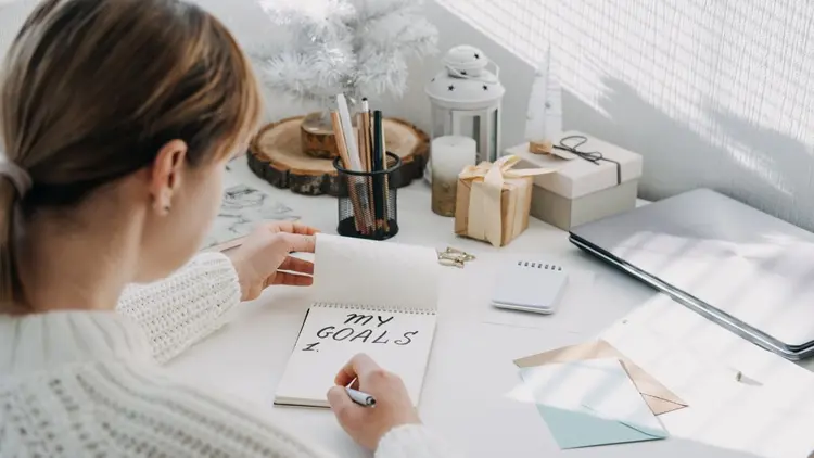 A woman sitting at her desk and writing her goals in a notepad.