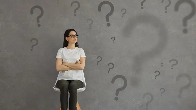A woman sitting on a chair, deep in thought with question marks in the background.