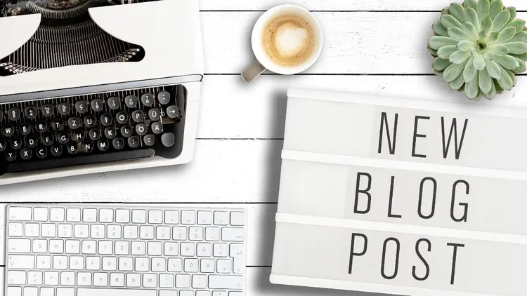 A desktop with an old typewrite and a cup of coffee with the words: "new blog post " written on a notebook cover.