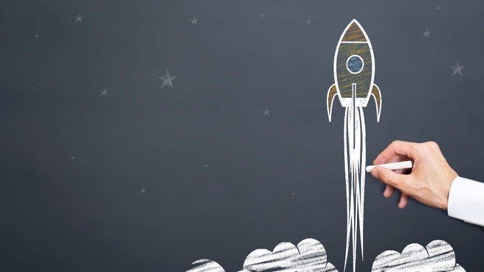 A person drawing a picture of a launching rocket on a blackboard.