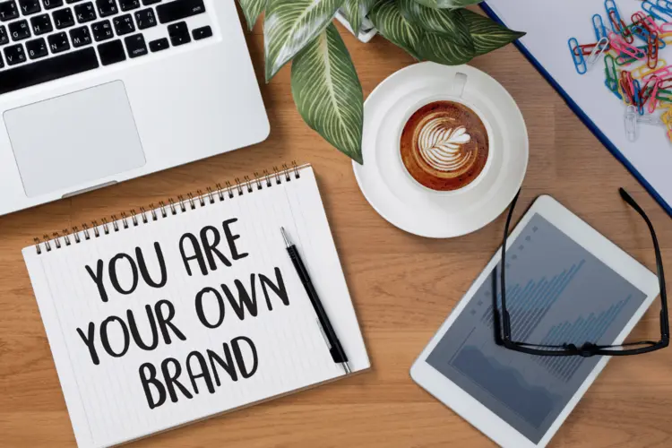 A laptop with a notepad with the words "You are your own brand" written on it.