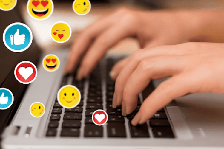 A person typing on a laptop with various emojis, depicting social media interaction.